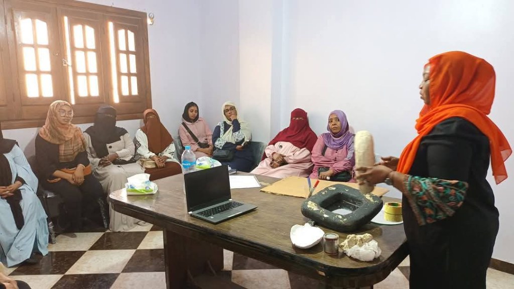 A group of women sitting around watching another woman decorate an object.